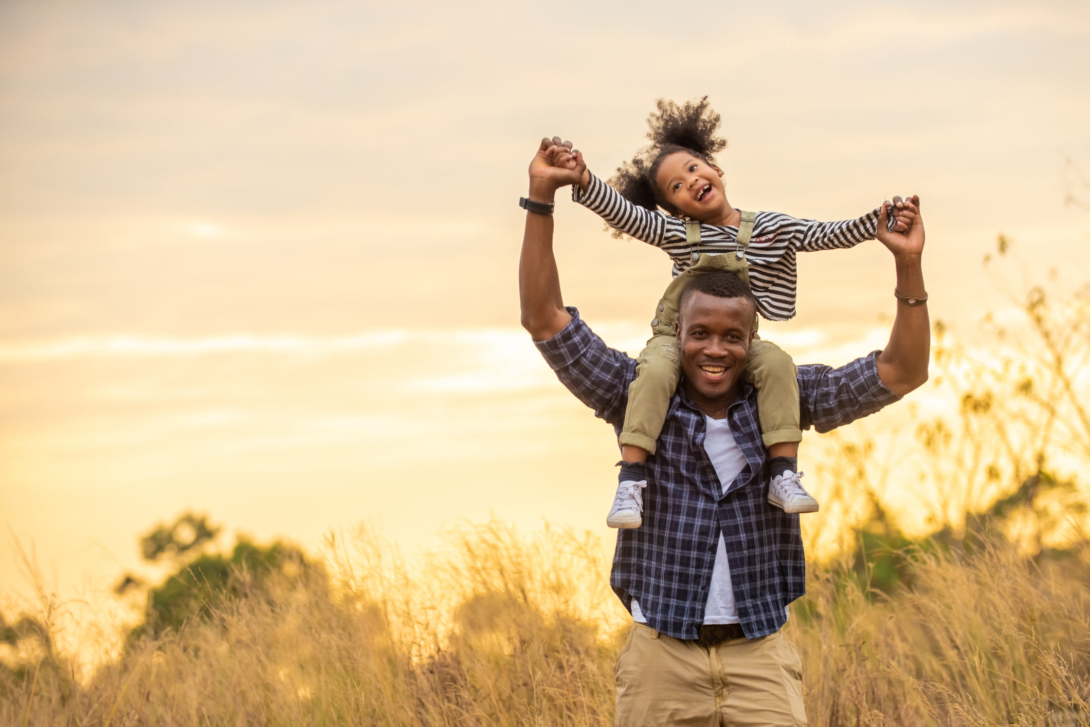 Father and his daughter on his shoulders, playing in a field during the golden hour.